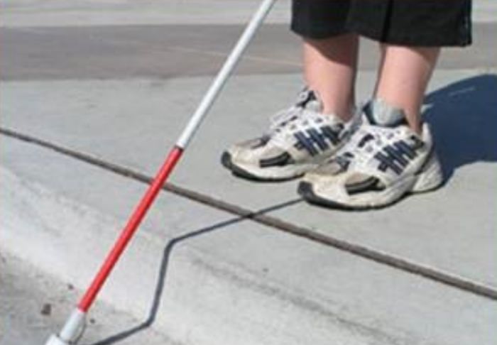 Photo of person standing at the edge of a curb with white cane