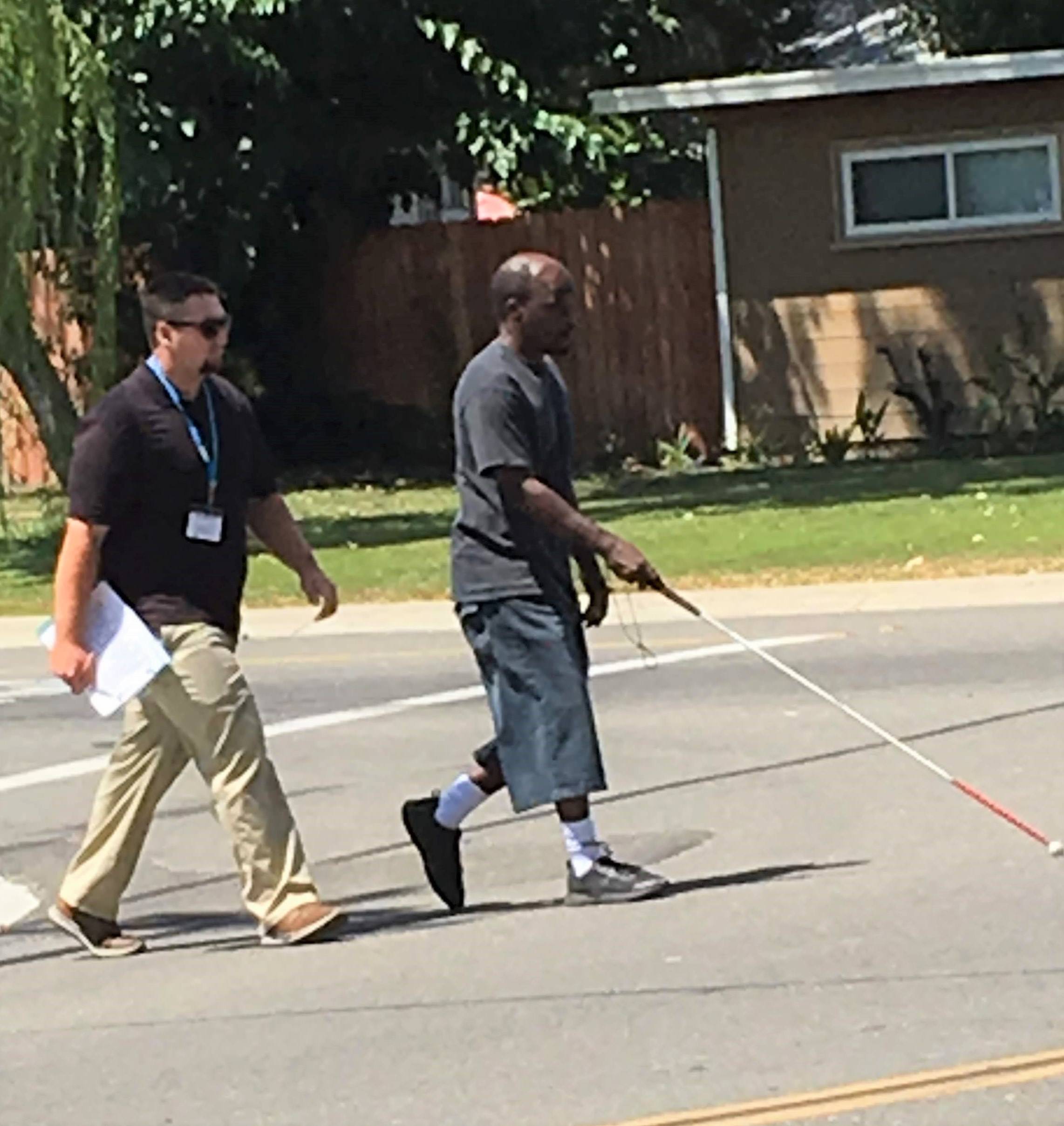 An orientation and mobility student crosses the street as his instructor follows.