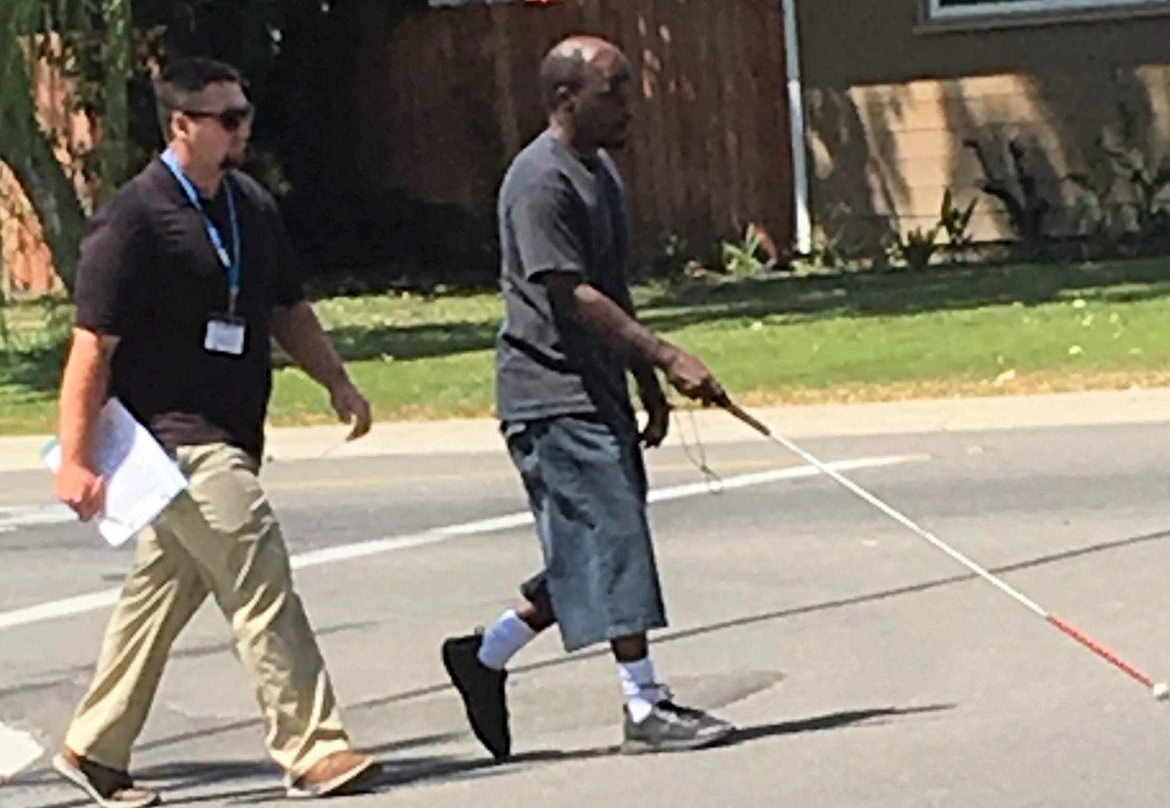 An orientation and mobility student crosses the street as his instructor follows
